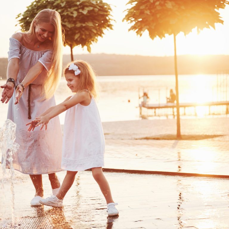 A woman playing with a child near the ocean in the park at sunset.